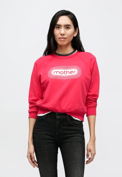 Raudonas džemperis su baltu ovaliu logotipu „mother“ centre. Raglan tipo rankovės, ribotas kaklo kraštas, dėvimas ant juodos palaidinės ir tamsių džinsų.