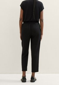 Schwarzer, lässiger Jumpsuit mit kurzen Ärmeln, elastischem Bund und schmal zulaufenden Beinen. Verfügt über zwei Gesäßtaschen und eine glatte Stoffoberfläche.