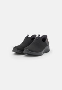 Black slip-on shoes with a textured knit upper, flexible rubber sole, and fabric accents at the heel. Features pull tabs for easy wear.