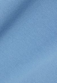 Vaaleansininen kangaspinta, jossa on hienovarainen neulontakuosi ja kevyitä laskoksia, jotka luovat pehmeitä varjoja pinnalle.