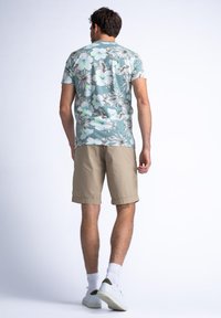 Korte mouwen overhemd in lichtblauw met een wit en grijs bloemenpatroon, gecombineerd met beige shorts en witte schoenen, gezien vanaf de achterkant.