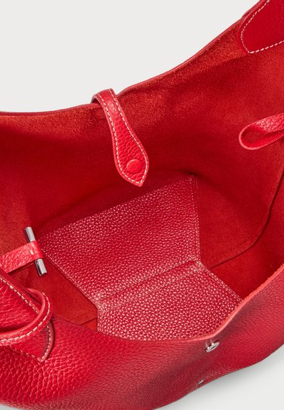 Sarkans ādas roku soma ar teksturētu virsmu, zamšādas oderi un metāla aksesuāriem. Aprīkota ar divām rokturiem un iekšējo kabatu.