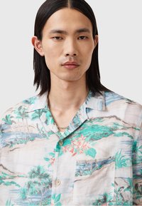 Camisa de manga corta con botones, fabricada en tejido ligero, que presenta un estampado de paisaje tropical en tonos turquesa, verde y coral.