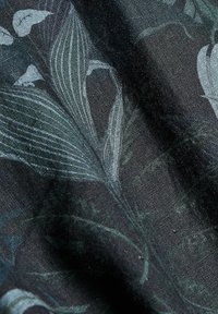 Tissu sombre avec de grands motifs botaniques subtils comprenant des feuilles et des formes de fleurs aux tons verts et gris atténués.