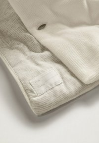 Tkanina w kolorze kremowym o fakturowanej, żłobkowanej powierzchni i gładkim spodzie. Zawiera wszytą etykietę informującą o rozmiarze i instrukcjach pielęgnacji.
