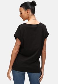 Camiseta de algodón negra con mangas cortas enrolladas y un corte holgado. La parte posterior tiene un dobladillo ligeramente curvado. Textura suave, diseño minimalista.