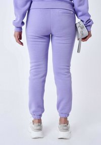 Lila sweatpants met een slim fit en afgeknipte enkels, gemaakt van zacht materiaal. Gepaarde met witte chunky sneakers en een kleine grijze tas.