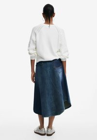 Vit tröja med strukturerade ärmar och en mörkblå, knälång denimkjol med utsvängd form och bakfickor. Silverfärgade sneakers.