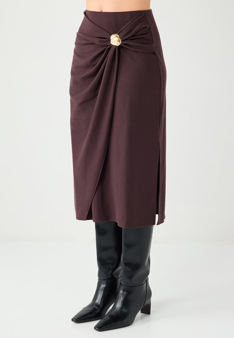 Maroon wrap skirt with a twisted front detail, featuring a gold accent. Made from soft fabric, it has a side slit and a fitted silhouette.