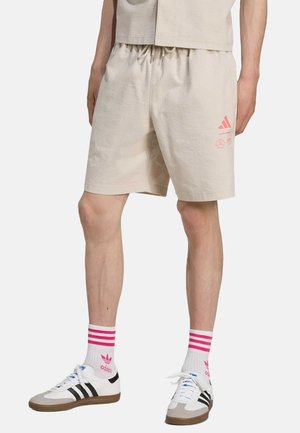 Beige teksturerede shorts med elastisk talje, prydet med lyserøde logo detaljer. Sammen med hvide sneakers og stribede lyserøde sokker.