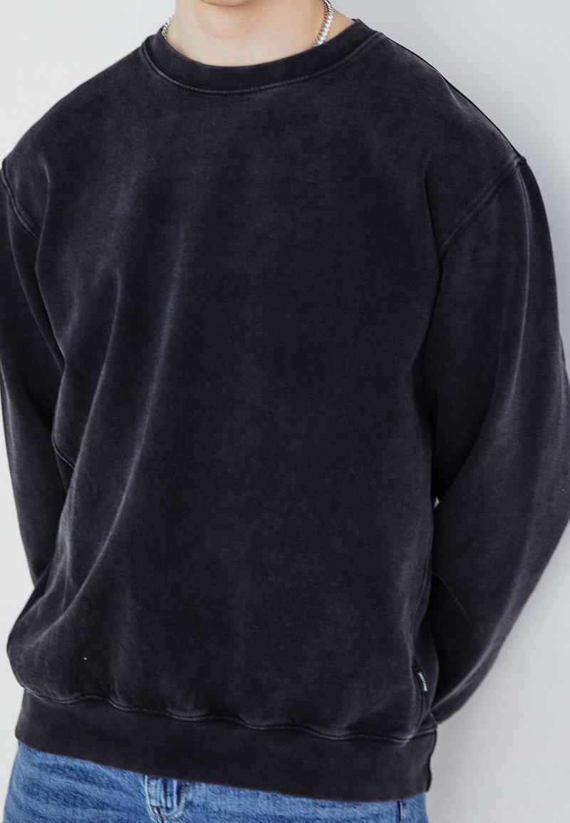 Černá bavlněná mikina s kulatým výstřihem, volným střihem a žebrovaným lemem. Má jemnou texturu a nenápadný opotřebovaný vzhled.