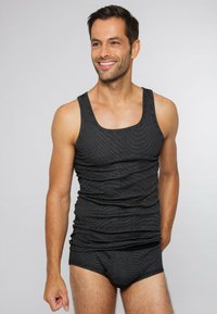 Zwart gestreept tanktopje met een ronde hals, gemaakt van zacht materiaal, gecombineerd met bijpassende zwarte slipjes. Model poseert zelfverzekerd.