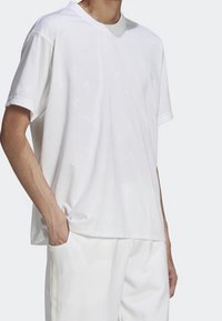 Bílý krátký rukáv tričko s jemným vzorem, vyrobené z lehkého materiálu, s kulatým výstřihem a volným střihem.