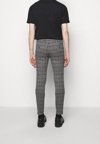 Pantalons à carreaux gris avec un motif à grille rouge, coupe slim, dotés de deux poches arrière, associés à des chaussures noires et un t-shirt noir.