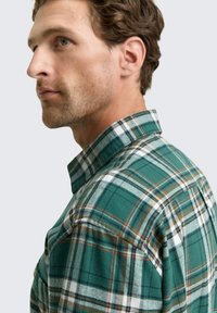 Groene geruite flanellen shirt met verschillende tinten groen, wit en bruin. Heeft een klassieke kraag en een knoopsluiting met een borstzakje.