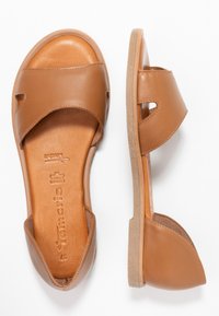 Sandalias de cuero marrón con un diseño de punta abierta, tiras anchas y suela plana. Plantilla texturizada y acentos recortados en los lados.