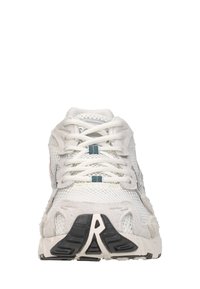 Witte sportschoen met mesh- en suèdeaccenten, witte veters en een zwart-beige zool met patroon, gezien vanaf de voorkant.