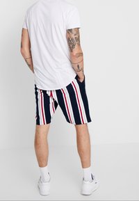 Shorts à rayures marines avec des rayures rouges et blanches, en tissu léger. Présente des poches et une coupe décontractée, associés à un t-shirt blanc.