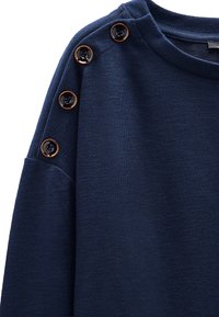 Granatowy sweatshirt wykonany z mieszanki bawełny, z ryflowanym dekoltem i dekoracyjnymi guzikami na ramieniu. Miękka tekstura i luźny krój.