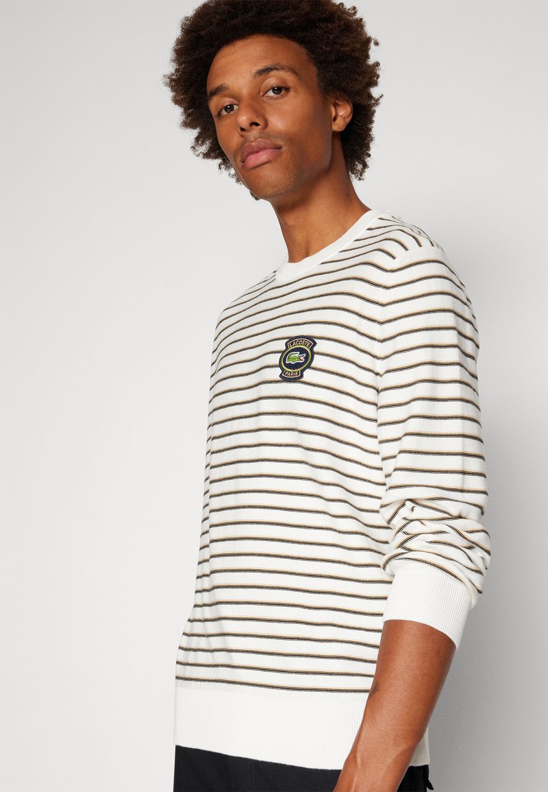 Gestreepte trui in het wit met bruine lijnen, met een ronde hals en geribbelde mouwen. Inclusief een geborduurd logo-detail aan de voorkant.