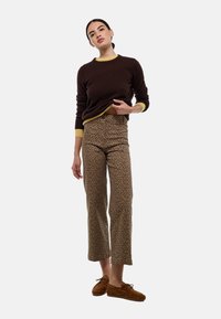 Un pull marron avec des accents jaunes, associé à un pantalon beige court ornés d'un imprimé léopard noir. Le modèle porte des chaussures en daim marron.