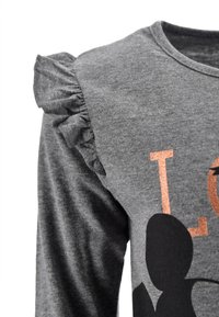 Una camiseta de manga larga gris presenta detalles con volantes en los hombros, una textura suave y un diseño impreso con acentos metálicos en naranja y negro.