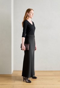 Haut noir à côtes avec fermeture éclair, jupe noire longue, chaussures à talons brillantes marron, et une pochette bourgogne foncé. Silhouette simple et élégante.