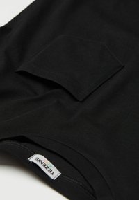 Czarny bawełniany t-shirt z kieszonką na piersi, gładką fakturą i delikatnie dopasowanym krojem. Metka widoczna przy dekolcie.