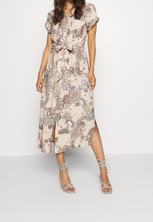 Kvinde iført en lys midi-kjole med et blomster-paisley mønster, korte ærmer, knapper foran, bælte i taljen og beige remsandaler med hæl.