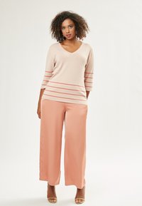 Maglione a scollatura a V in un delicato beige con strisce orizzontali rosse, abbinato a pantaloni a gamba larga color pesco. Tessuto morbido e vestibilità rilassata per tutto l'outfit.