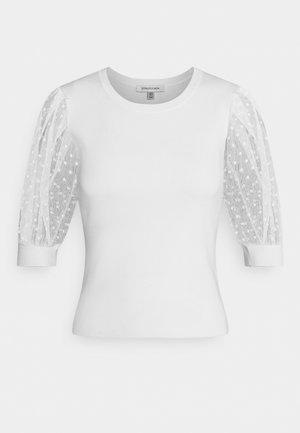 Haut blanc ajusté à col rond, avec des manches trois-quarts bouffantes et transparentes à petits pois.