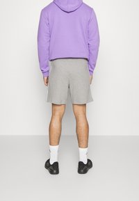 Grå sportshorts med sidostrepen, kombinerat med en lavendelfärgad hoodie. Personen har svarta skor och vita strumpor, sedd från bakom.