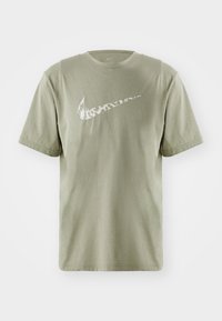 Olíva zöld pamut póló rövid ujjakkal és kerek nyakkal. A mellkason egy textúrált mintázatú fehér Nike swoosh logó található.