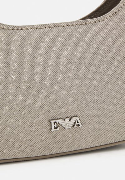 Béžová texturovaná kabelka vyrobená z syntetického materiálu, s výrazným stříbrným logem EVA a decentním prošitím podél okrajů.