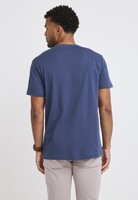 Marinblå bomull t-shirt med korta ärmar, rund halsringning och en jämn textur, båda med ljusa byxor och ett mörkt armbandsur.