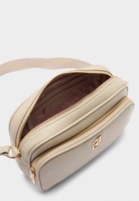 Borsa a tracolla beige chiaro realizzata in materiale liscio, dotata di due scomparti con zip, hardware dorato e una fodera interna morbida.