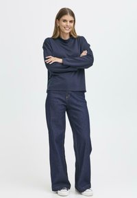 Mörkblå långärmad topp kombinerad med högmidjade, vida denimjeans. Slät textur, kontrasterande sömnadsdetaljer och avslappnade sneakers.
