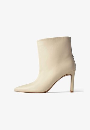 Beżowy skórzany botek za kostkę z ostrym noskiem, smukłym obcasem w kształcie szpilki i gładką teksturą; posiada subtelny tylny szew jako dodatkowy detal.
