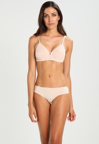 Beige polstret bh med justerbare stropper og en enkel underwire-design, paret med matchende bikini-stil truse. Glatt tekstur, uten mønstre.
