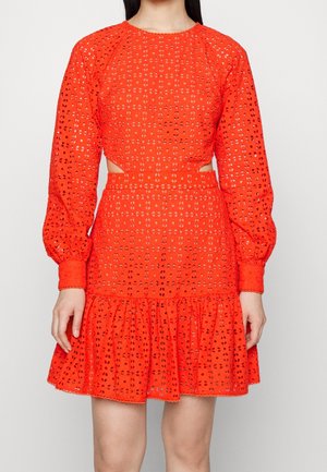 Woman wearing a bright orange eyelet lace dress with long puffed sleeves, cut-out waist, and a ruffled hem above the knee.