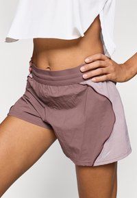 Pantalones cortos para mujer de Nike con diseño bicolor en malva y morado claro, cinturilla elástica y logotipo reflectante en el lateral.