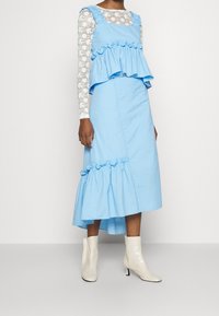 Ljusblå randig klänning med volang i midjan, axelband och utsvängd nederkant, kombinerad med vita, glansiga ankelstövlar.