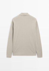 Polo met lange mouwen in licht beige, gemaakt van zacht stof. Voorzien van een standaardkraag, knoopsluiting en rechte zoom.