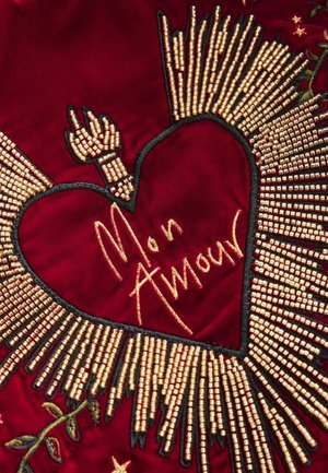 Red fabric featuring a heart shape with intricate golden beadwork and embroidery. The text "Mon Amour" is displayed in gold.