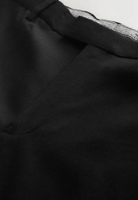 Čierna tkanina s jemnou textúrou, s výstrihom do V a hladkým vnútorným podšívkam. Dizajn zobrazuje čisté stehy a švy.