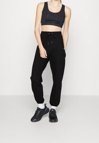 Top atlético negro corto con tejido texturizado, combinado con joggers negros de corte holgado que tienen cordón y puños en los tobillos, usados con zapatillas negras.