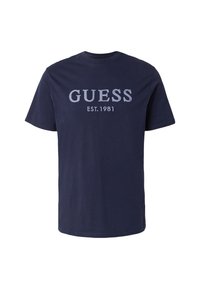 Camiseta de algodón de manga corta en azul marino, con las palabras "GUESS" y "EST. 1981" en texto gris claro en contraste en la parte delantera.