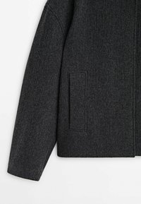 Veste gris foncé, texturée, avec une coupe droite, dotée d'une poche à rabat unique et d'un design minimaliste. Matériau doux semblable à de la laine.