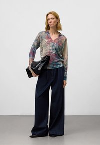 Chemisier transparent multicolore avec un col en V et des manches longues, associé à un pantalon en denim foncé à jambes larges et un sac noir. Motif de petits pois subtil.
