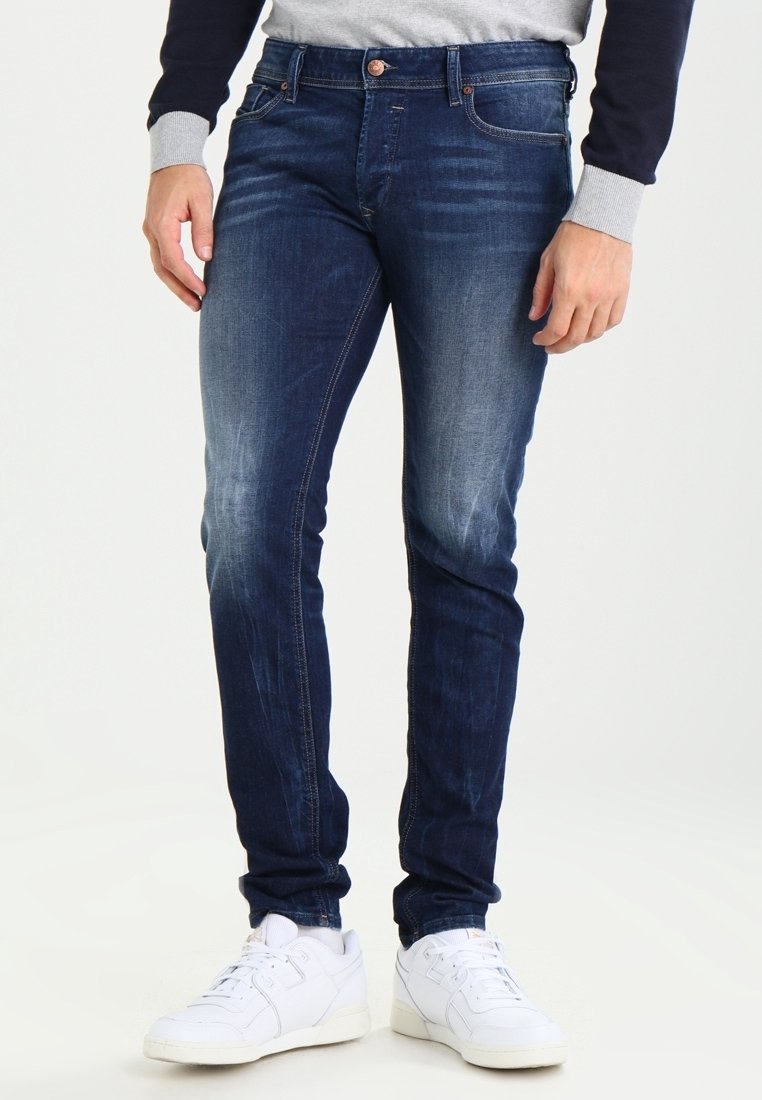 Mörkblå denimjeans med slim fit, med ljus blekning, fem fickor och kontrastfärgade sömmar. Bärs med vita sneakers.